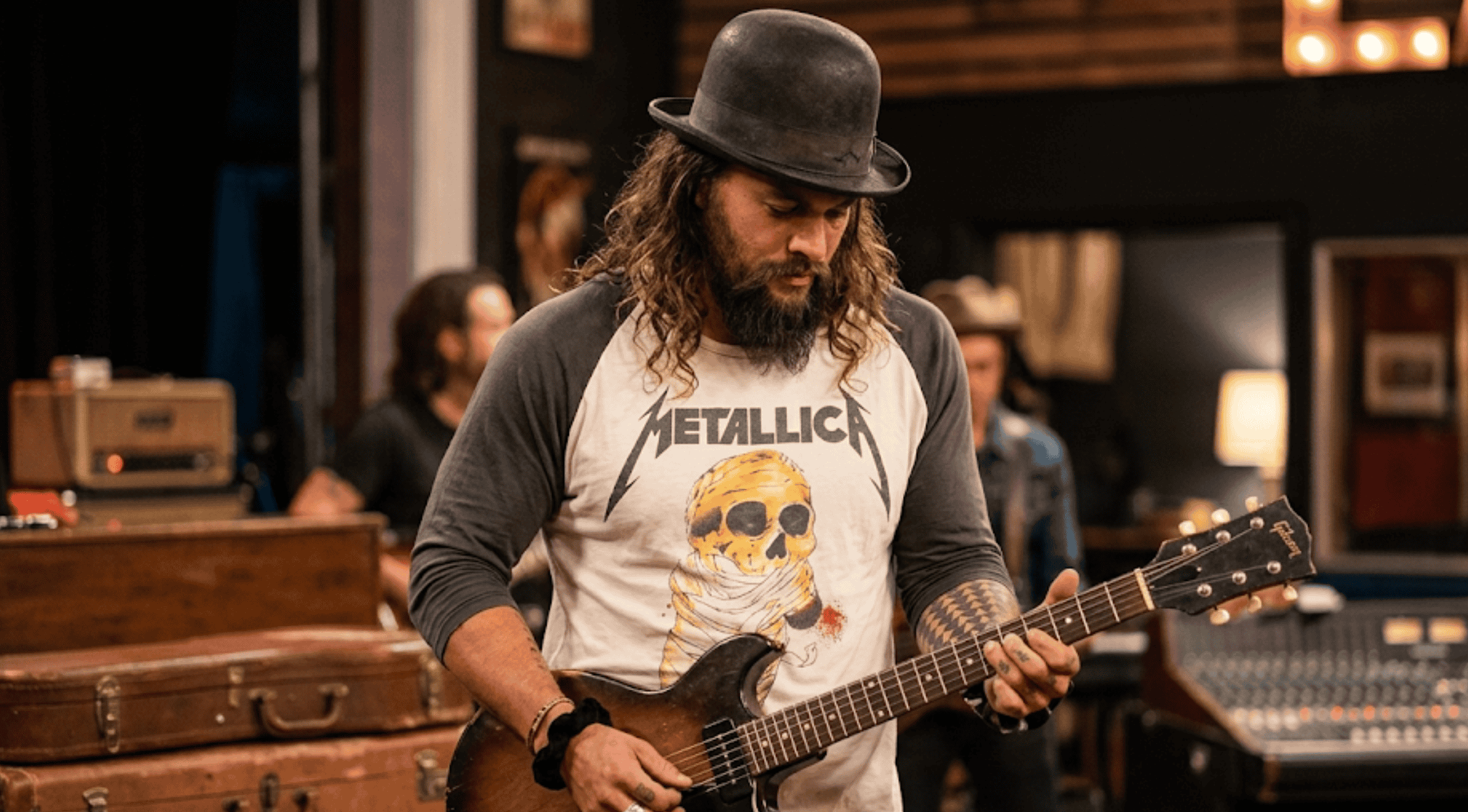 Jason Momoa playing guitar wearing On the Roam Metallica skull graphic two-tone raglan t-shirt
